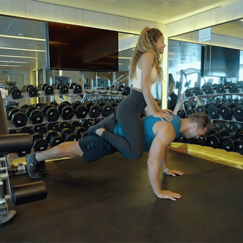 A Man Is Doing Push Ups With A Woman Riding On His Back GIF