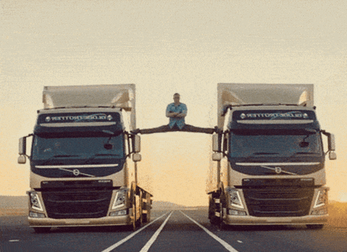 A Man Is Doing Splits Between Two Volvo Trucks On A Highway GIF