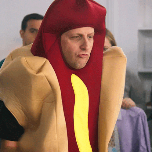 A Man Is Dressed As A Hot Dog With A Yellow Stripe GIF