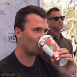 A Man Is Drinking A Cup Of Coffee While Another Man Stands Behind Him . GIF