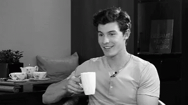 A Man Is Drinking A Cup Of Coffee While Sitting In A Chair . GIF