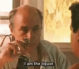 A Man Is Drinking A Glass Of Liquor And Talking To Another Man . GIF