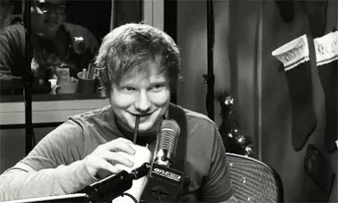 A Man Is Drinking A Milkshake Through A Straw In Front Of A Microphone . GIF