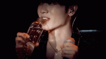 A Man Is Drinking From A Bottle While Holding A Microphone . GIF