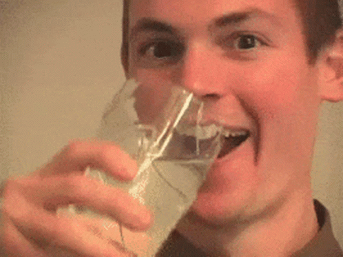 a man is drinking from a glass and smiling with his tongue out .