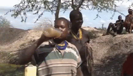 A Man Is Drinking Water From A Bottle While Another Man Sits On A Rock . GIF