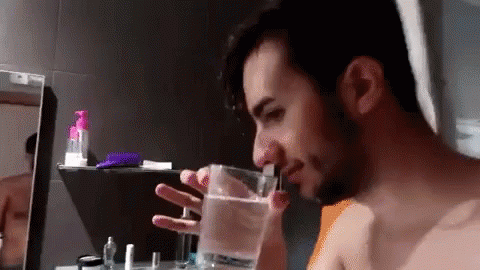 A Man Is Drinking Water From A Glass In A Bathroom . GIF