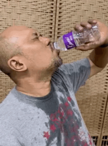 A Man Is Drinking Water From A Plastic Bottle With A Purple Label GIF