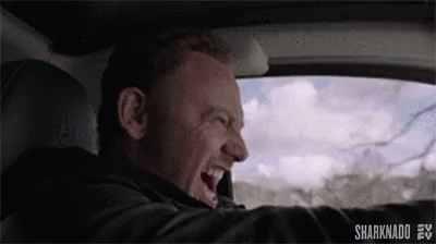 A Man Is Driving A Car And Laughing While Looking Out The Window . GIF