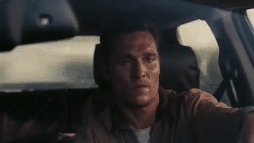 A Man Is Driving A Car And Looking At The Camera . GIF