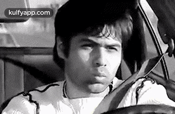 A Man Is Driving A Car And Making A Funny Face In A Black And White Photo . GIF