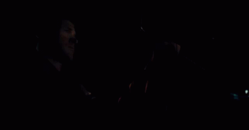 A Man Is Driving A Car At Night And Holding The Steering Wheel In His Hand . GIF