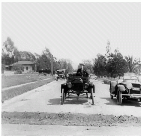 A Man Is Driving A Car Down A Street Next To A Convertible Car . GIF