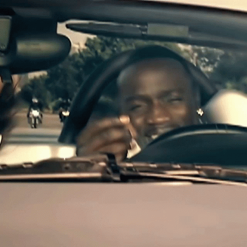 A Man Is Driving A Car While Holding A Cigarette In His Mouth GIF