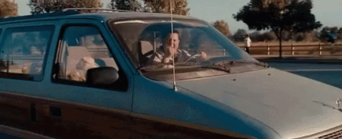 A Man Is Driving A Minivan Down A Road While Talking On A Cell Phone . GIF