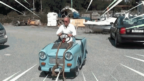 A Man Is Driving A Small Blue Car With A Rope Attached To The Front Of The Car GIF