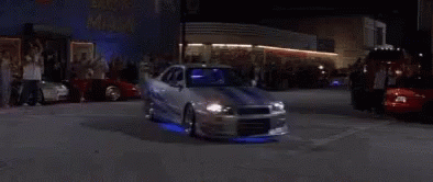 A Man Is Driving A Sports Car At Night In A Garage . GIF