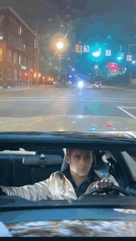 A Man Is Driving Down A Street At Night With A Sign That Says A On It GIF