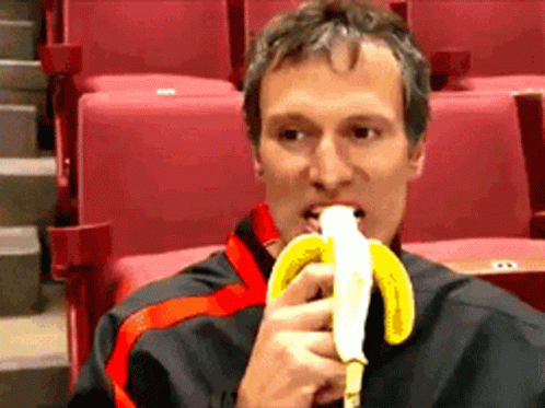 A Man Is Eating A Banana In A Theater GIF