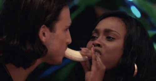 A Man Is Eating A Banana While A Woman Holds A Banana To His Mouth GIF