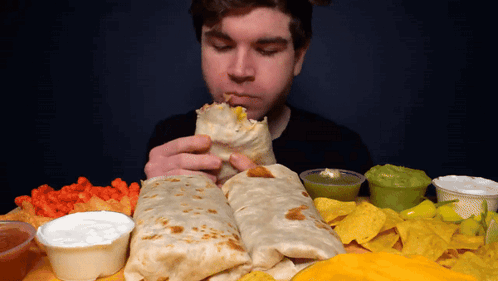 A Man Is Eating A Burrito Surrounded By Nachos And Sauces GIF
