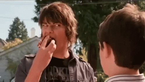 A Man Is Eating A Donut While Another Man Watches . GIF