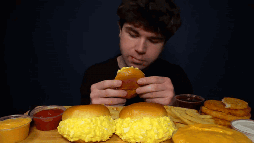 A Man Is Eating A Hamburger And French Fries At A Table GIF