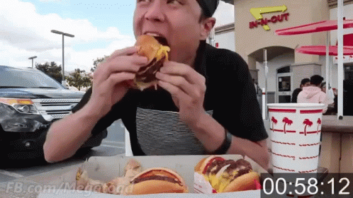A Man Is Eating A Hamburger In Front Of An In N Out Restaurant GIF