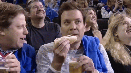 A Man Is Eating A Hot Dog And Drinking Beer While Watching A Game GIF