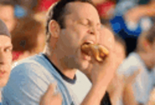 A Man Is Eating A Hot Dog In A Crowd Of People At A Sporting Event . GIF