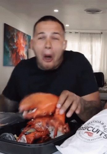 A Man Is Eating A Large Lobster With A Bag Of Biscuits In Front Of Him GIF