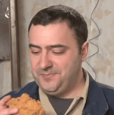 A Man Is Eating A Piece Of Fried Chicken While Looking At The Camera . GIF