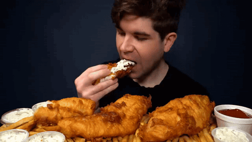 A Man Is Eating A Piece Of Fried Chicken With Ranch Dressing GIF