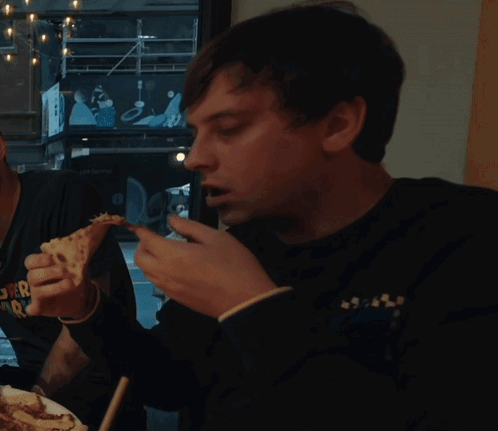 A Man Is Eating A Slice Of Pizza While Wearing A Shirt That Says " Super Radio " GIF