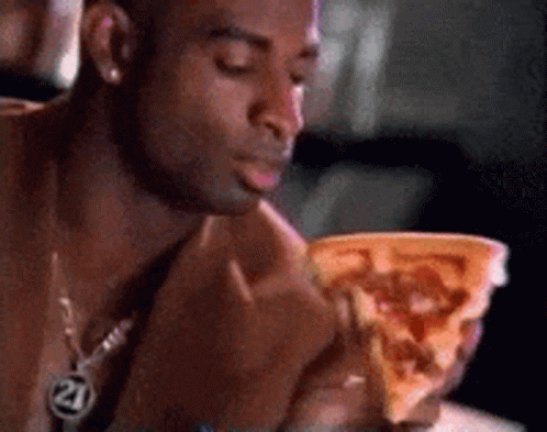 A Man Is Eating A Slice Of Pizza With The Number 21 On His Neck GIF