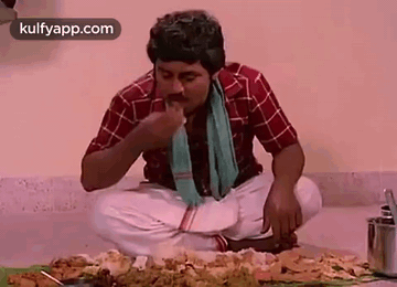A Man Is Eating Food While Sitting On The Floor . GIF