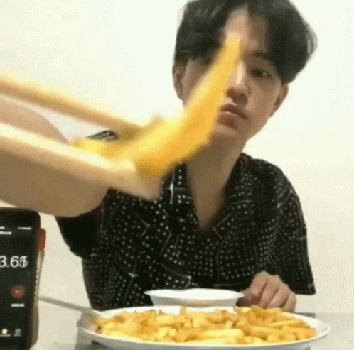 A Man Is Eating French Fries With Chopsticks And A Cell Phone In The Background . GIF