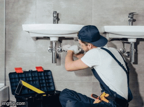 A Man Is Fixing A Sink In A Bathroom With A Toolbox Next To Him GIF
