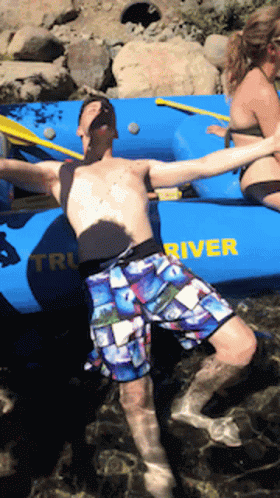 A Man Is Floating In The Water Near A Boat That Says River GIF