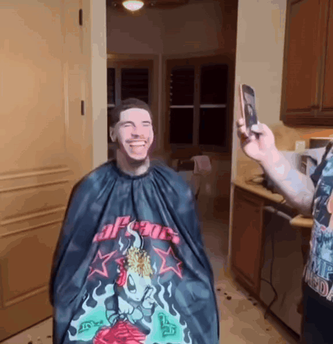 a man is getting his hair cut by a man wearing a cape that says apsoc on it