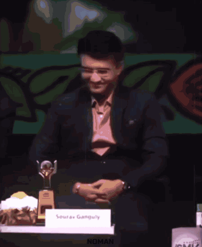A Man Is Giving A Speech At A Podium And The Word Noman Is On The Screen Behind Him GIF