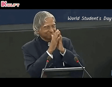 A Man Is Giving A Speech In Front Of Microphones And The Words World Student 'S Day Are On The Screen Behind Him GIF