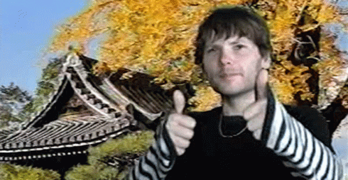 A Man Is Giving A Thumbs Up In Front Of A Tree And A Building GIF