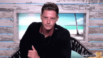 A Man Is Giving A Thumbs Up While Sitting In A Chair In Front Of A Window . GIF