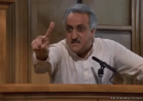 A Man Is Giving The Middle Finger While Standing In Front Of A Microphone In A Courtroom . GIF