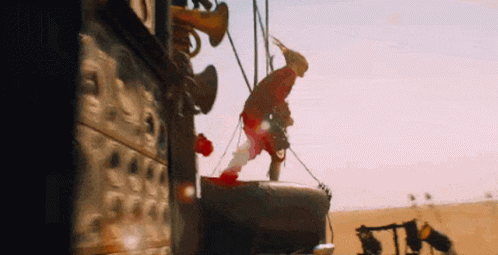 A Man Is Hanging From A Rope In The Desert While Wearing A Hat . GIF