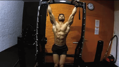 A Man Is Hanging Upside Down On A Bar In A Gym . GIF