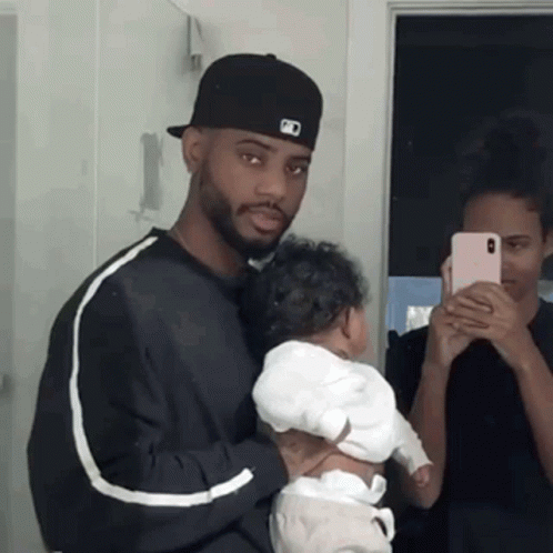 A Man Is Holding A Baby In Front Of A Mirror While A Woman Takes A Picture Of Them . GIF
