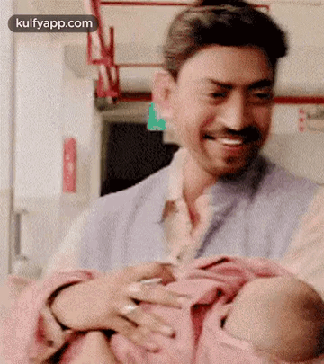 A Man Is Holding A Baby In His Arms While Smiling . GIF