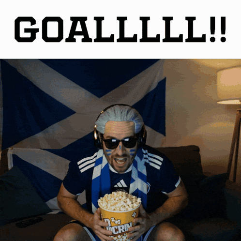 A Man Is Holding A Bag Of Popcorn With The Words Goallll !! Behind Him GIF